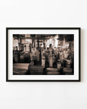Antique medicine bottles and faded remedy labels in a crowded cabinet, photographed in sepia.