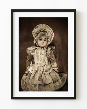 Antique porcelain doll wearing a lace bonnet and layered dress in warm sepia tones.
