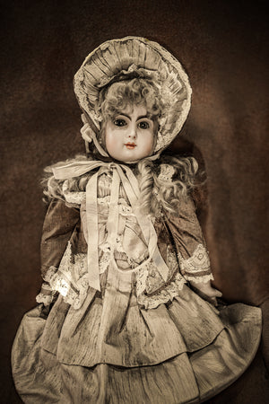 Warm toned portrait of an antique porcelain doll with a broad lace bonnet.