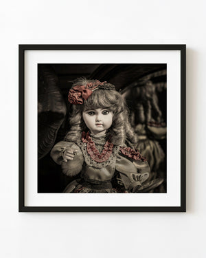 Antique porcelain doll with curled hair and muted red ribbons against a dark background.