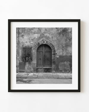 Arched wooden double door in a weathered Tuscan facade, photographed in black and white.