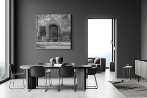 Worn plaster and an arched stone entrance frame a Tuscan wooden double door.