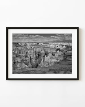 Tall Arizona canyon cliffs and deep rock channels beneath clouds in black and white.