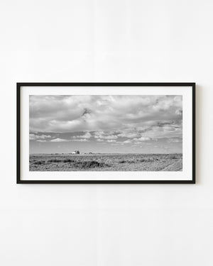 A solitary Arizona homestead sits beneath a vast cloudy sky in black and white.