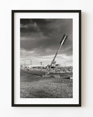 An oversized metal arrow leans across the sky near Flagstaff, Arizona, in black and white.