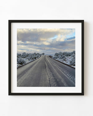 An empty Arizona road runs between snow dusted shrubs beneath layered winter clouds.