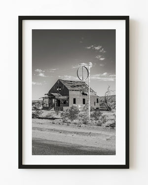 An empty circular sign frame above a ruined building on Arizona’s Route 66 in black and white.
