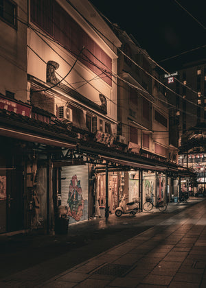 Amber light falls across shopfronts and pavement on a narrow Asakusa street at night.