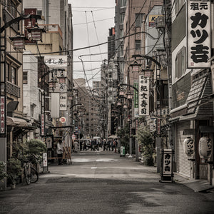 A Tokyo lane leads between shopfronts and hanging lanterns toward a distant crossing.