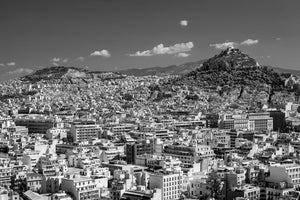 Monochrome cityscape of pale Athens buildings with a prominent rocky hill in the distance.