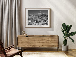 Closely packed buildings and roof terraces stretch below a rocky Athens hillside.
