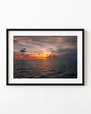 Orange sunset light reflects across the Atlantic Ocean beneath layers of grey and pink clouds.