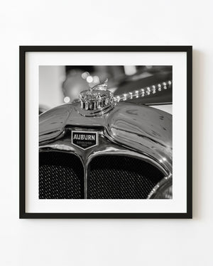A vintage Auburn hood ornament rises above its badge and twin mesh grille openings in black and white.