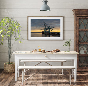 Colour industrial photograph of blue cranes, a ship and stacked containers at sunset.