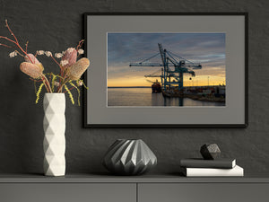 Blue steel cranes contrast with yellow sunset light across an Australian working harbour.