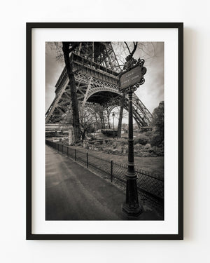 An ornate Avenue Gustave Eiffel sign stands before the Eiffel Tower in black and white.