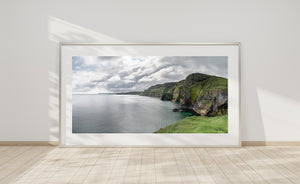 Dark rock faces and bright green grass contrast with pale water along the Ballintoy coast.