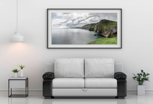 Soft grey and white clouds stretch over a quiet sea beside Northern Ireland’s rugged shoreline.
