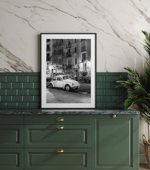 Vertical monochrome street scene combining a classic Volkswagen Beetle with balconies and shuttered Barcelona shops.