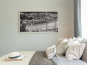 Framed black and white cityscape print on a wall above a bed with pillows.