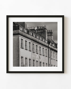 Chimney pots and dormer windows rise above pale Bath stone facades in black and white.