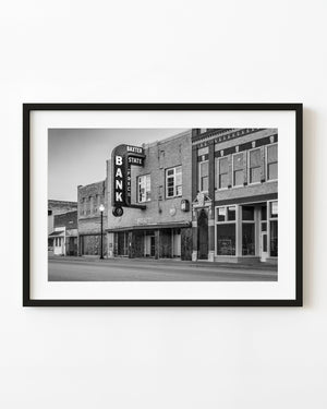 Baxter State Bank’s vertical sign projects above a quiet Route 66 street in black and white.