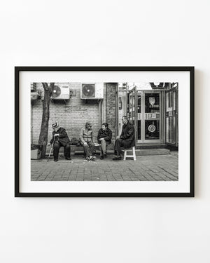 Four older neighbours sit outside a Beijing restaurant in black and white.