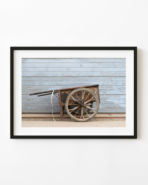 Rusted metal wheelbarrow against a pale blue shutter in Beijing