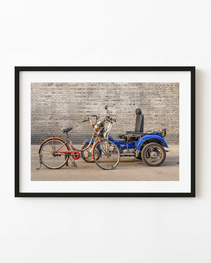 Rusty bicycle and blue motorized cart against a grey brick wall in Beijing