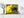 Dark-furred bear cub against a softly blurred yellow-green forest.