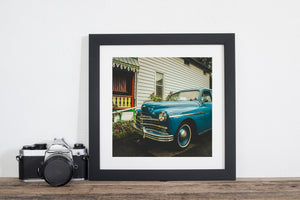 Chrome trim catches light on a blue Plymouth parked beside a porch.