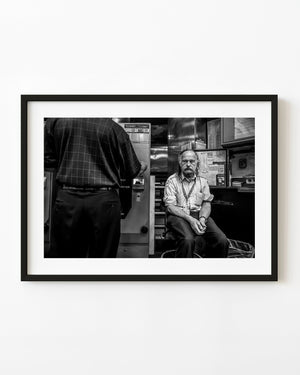 Boston subway worker seated beside station machinery in black and white