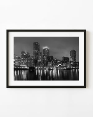 Boston waterfront at night with illuminated buildings reflected on harbour water in black and white