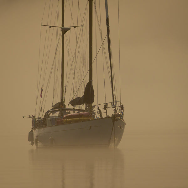 Serene sailboat scene in British Columbia, bathed in warm, early morning sunlight amidst a misty backdrop.