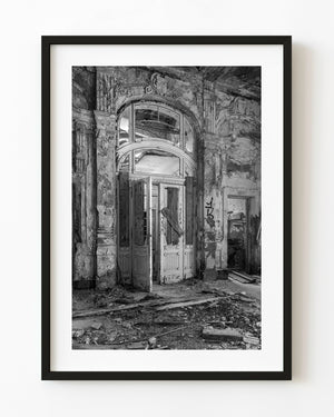 Broken doors beneath an ornate abandoned hotel arch in Zagreb, photographed in black and white.