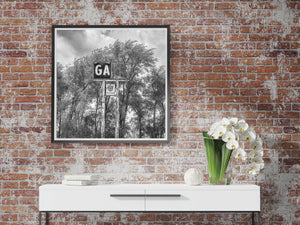 Pale letters remain on a broken gas sign supported by tall posts among trees.
