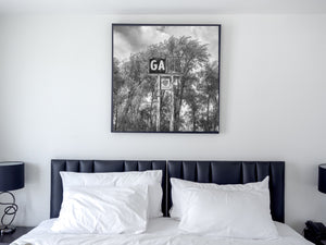 Tall gas sign posts descend through foliage beneath a damaged dark panel.