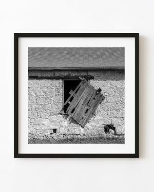 Broken wooden shutter on an old stone barn, photographed in black and white.