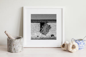 Rustic architectural detail of a broken shutter on a stone barn wall.