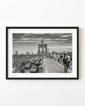 Pedestrians and traffic crossing Brooklyn Bridge in New York City, photographed in black and white.