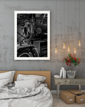 Black and white railway detail with curved pipes, bolts and dark metal surfaces.