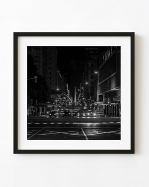 Black and white Buenos Aires night photograph with headlights and the distant Obelisk.