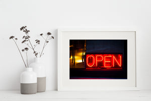 Red neon tubing spells OPEN beside a warmly lit window at night.