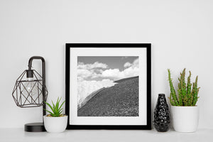 Square black and white mountain photograph of white snow against a rocky slope.