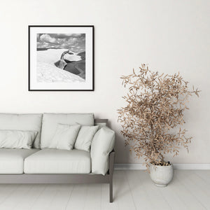 Square black and white photograph of melting snow and a small alpine pond.