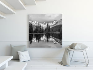 Black and white lake reflection of rugged mountain spires and evergreen forest.