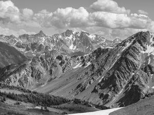Layered Bugaboo mountain peaks and snow patches beneath bright clouds.