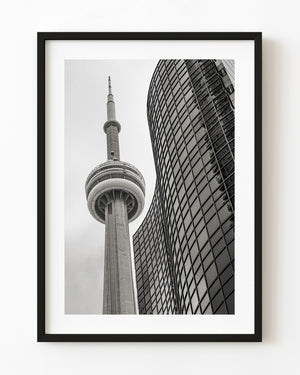 Black and white Toronto photograph of the CN Tower beside a curved glass building viewed from below.