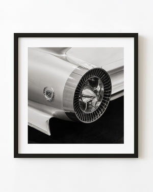 Black and white close-up of a classic Cadillac’s circular chrome rear detail and sculpted bodywork.
