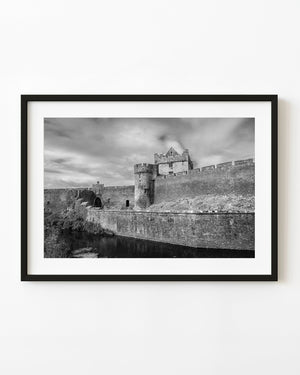Black and white photograph of Cahir Castle’s outer stone walls and tower beneath a cloudy sky.